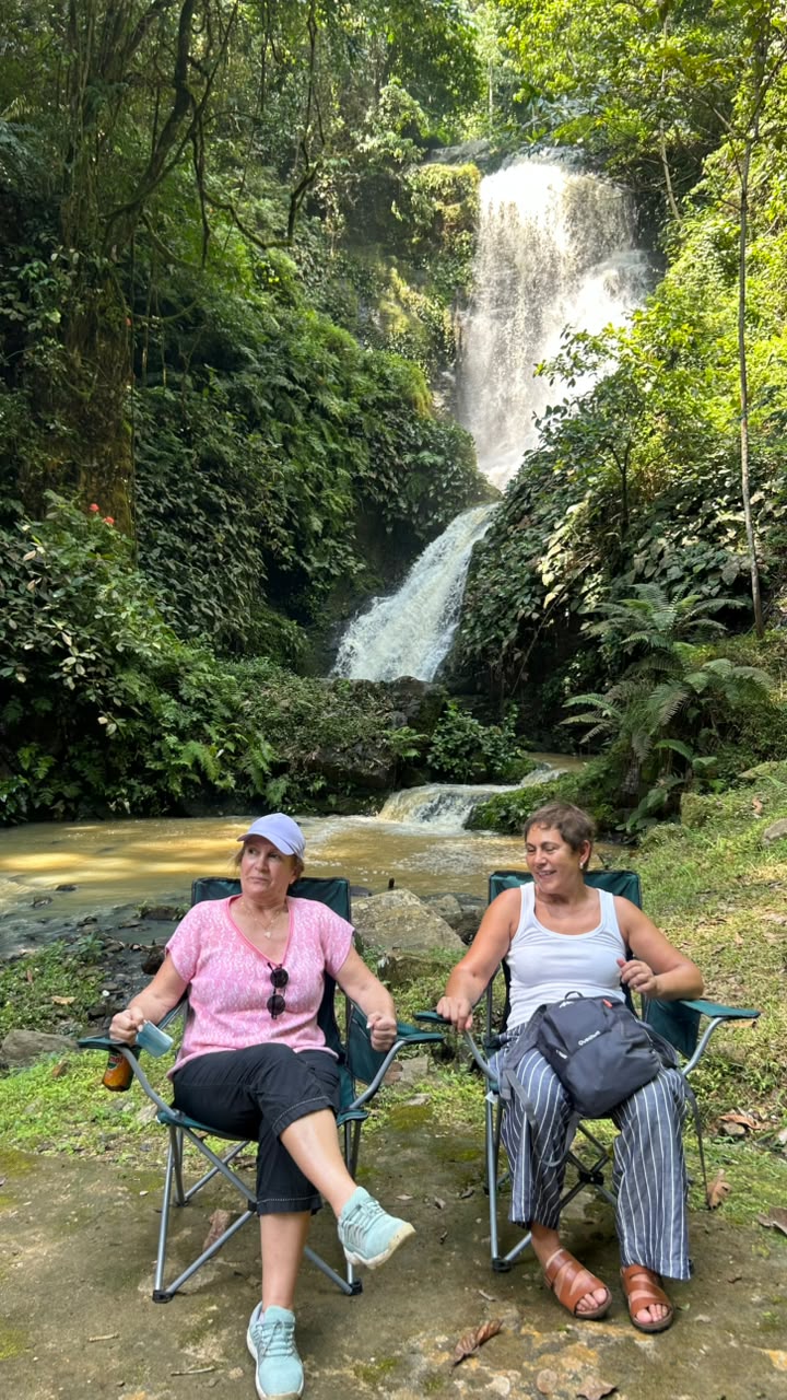 Duas visitantes sentadas perante uma cascata tropical